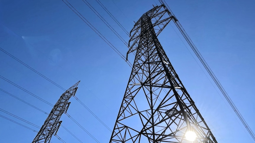 View directly up at two, high-voltage transmission poles shot from the ground up, blue sky in background