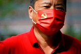 A man stares as he wears a red face mask with the CCP flag on the left hand corner.