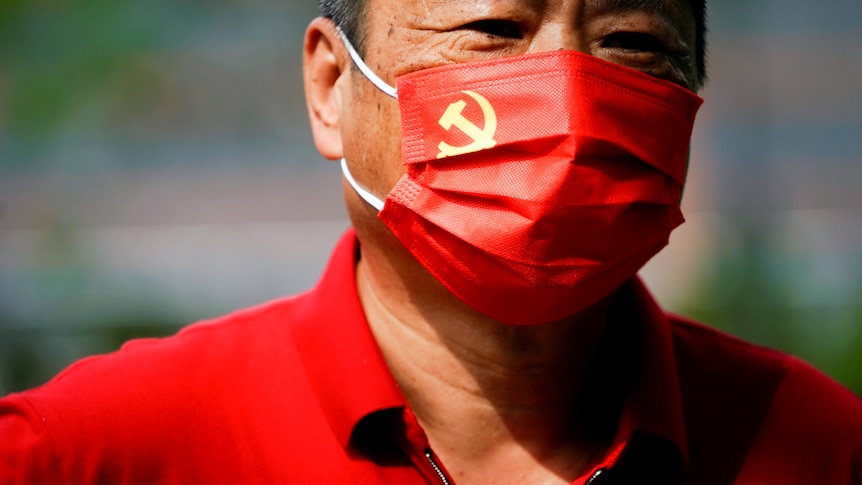 Un hombre mira mientras lleva una máscara roja con la bandera del PCCh en la esquina izquierda.