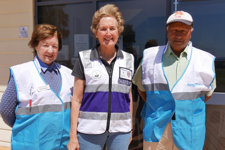 Three volunteers, two women, and one man in vests smile at a camera.