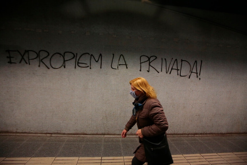 A woman walks through a dark pedestrian subway with graffiti that reads 'expropiem la privada!'