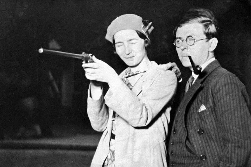 Simone de Beauvoir holding a gun, eyes closed, and Jean-Paul Sartre with pipe in mouth.