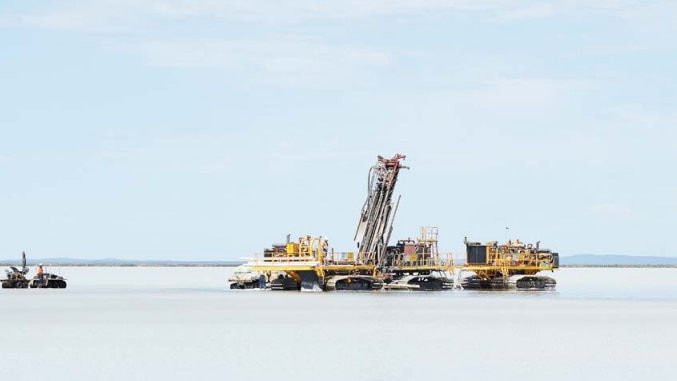 An drilling machine on a lake, blue sky with clouds, a drill in themiddle and two small boats on the side.