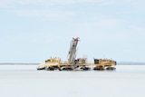 An drilling machine on a lake, blue sky with clouds, a drill in themiddle and two small boats on the side.