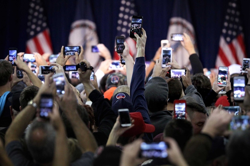 A sea of hands hold up their phone cameras as they wait for the arrival of Donald Trump.