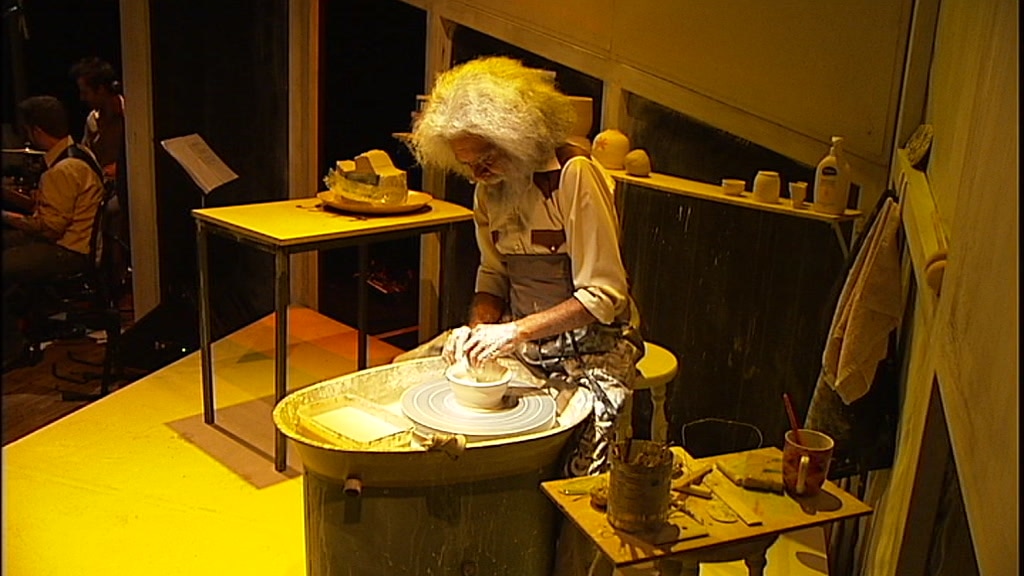 Uncle Jack Charles works at a pottery shelf on stage under yellow lighting.