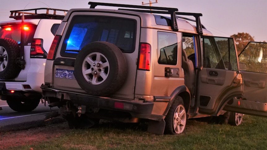 A gold 4WD on the side of the road with doors open and a police be