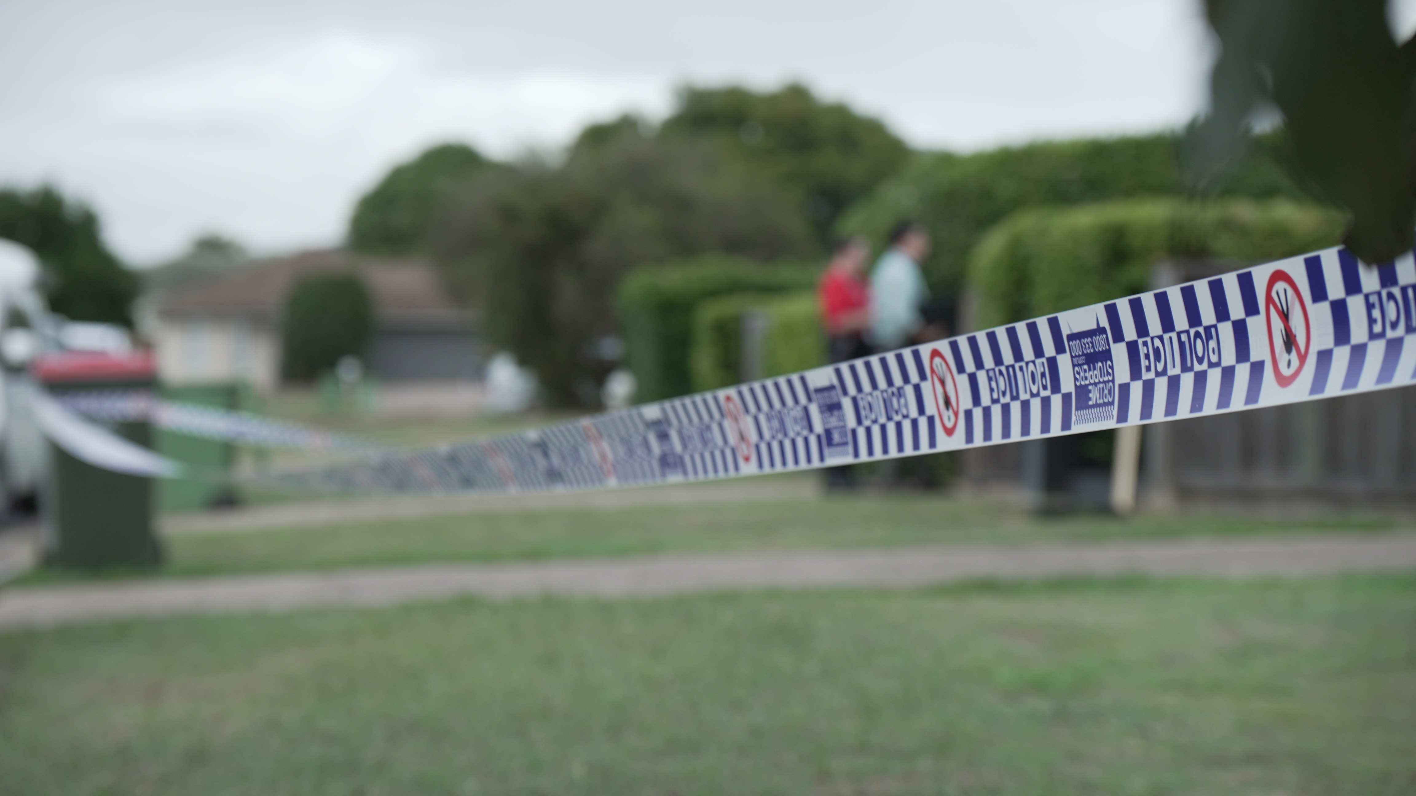Blue and white Queensland police tape across a lawn.