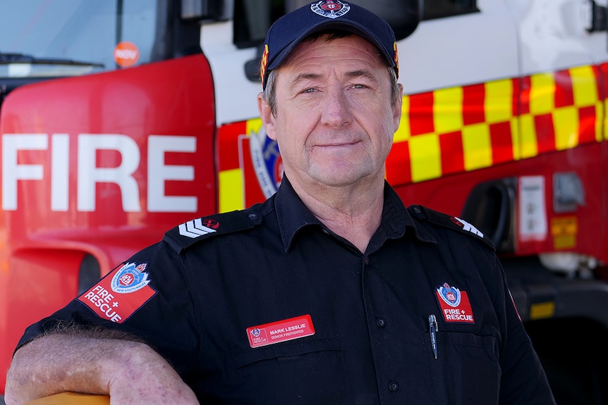Mark Lesslie stands in front of a fire truck in his Fire and Rescue NSW casual uniform.