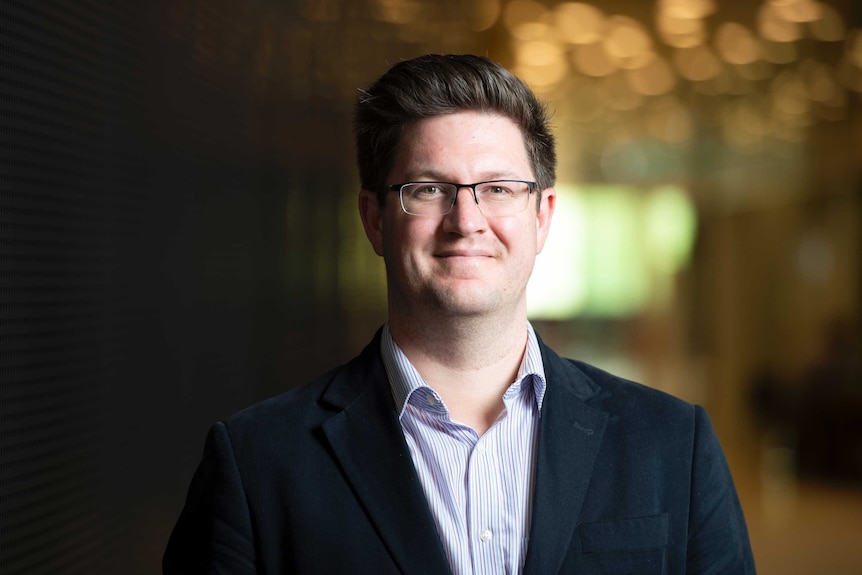 A picture of a man in a suit with glasses smiling at the camera.