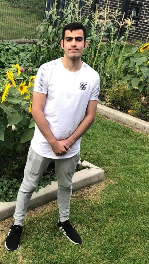 A young man in a white shirt stands in a garden