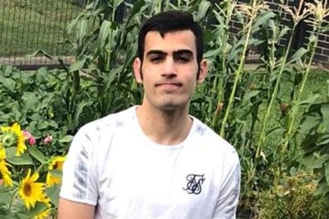 A young man in a white shirt stands in a garden