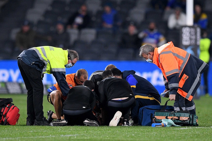 A Wests Tigers NRL player lies on the ground as he is attended to by medical officials.