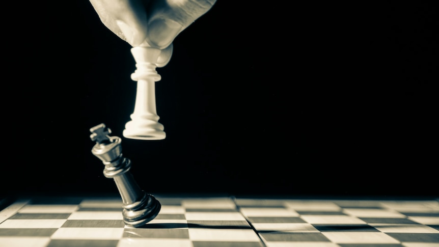 A photo of a chessboard with the white queen knocking over the black king