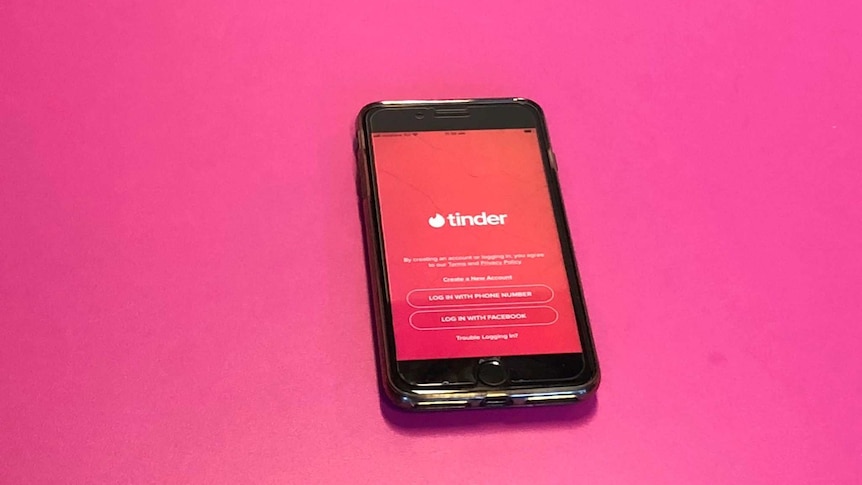A mobile phone on a pink table with the Tinder application open on the screen