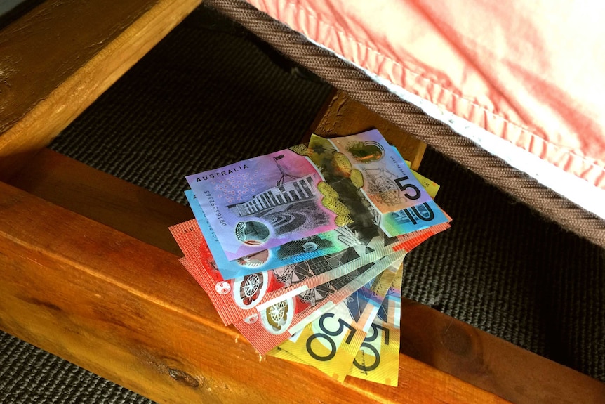A number of bank notes of different denominations sitting on a bed frame under a raised mattress.