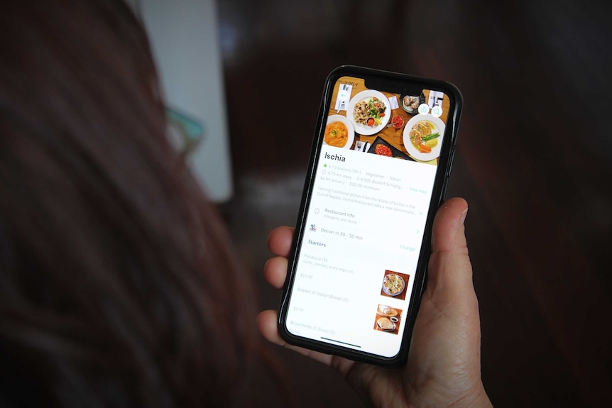 A woman looks at a phone displaying food delivery options