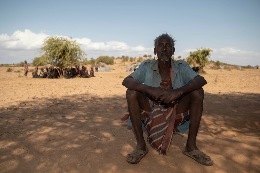 An older Ethiopian man wearing an open shirt sits on dry earth