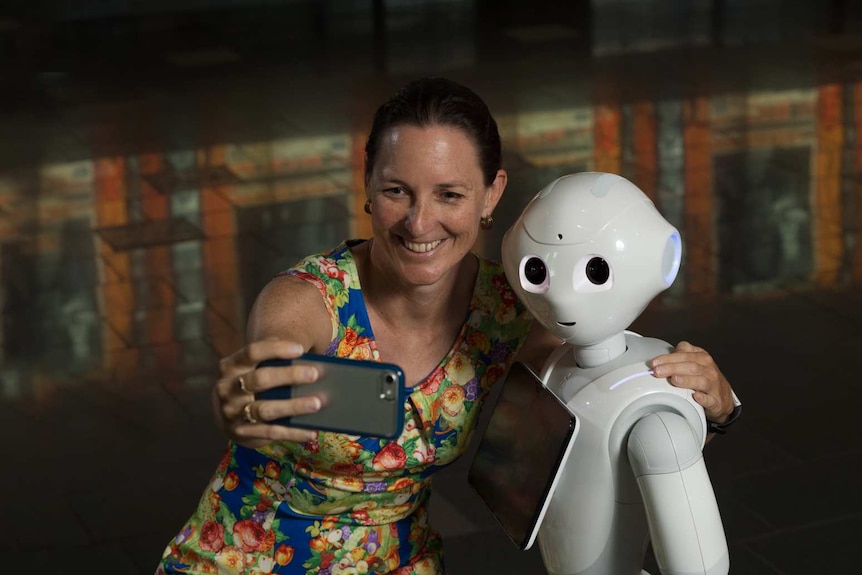 A woman taking a selfie with a life sized robot.