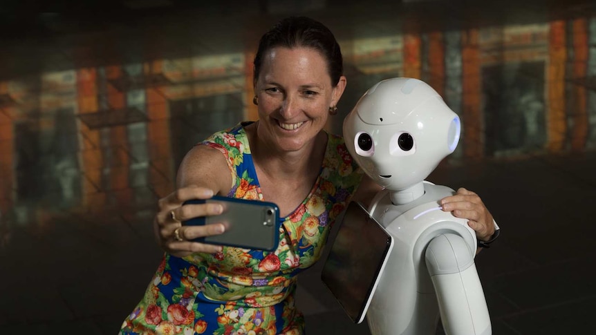 A woman taking a selfie with a life sized robot.