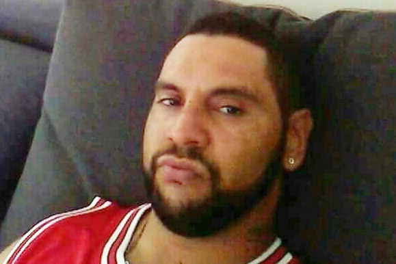 Man with beard and ear piercing stares at camera as he reclines on lounge.