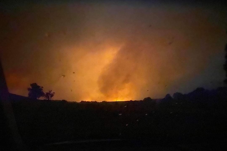 A view through a windscreen of a smoky sky with fire in the distance 