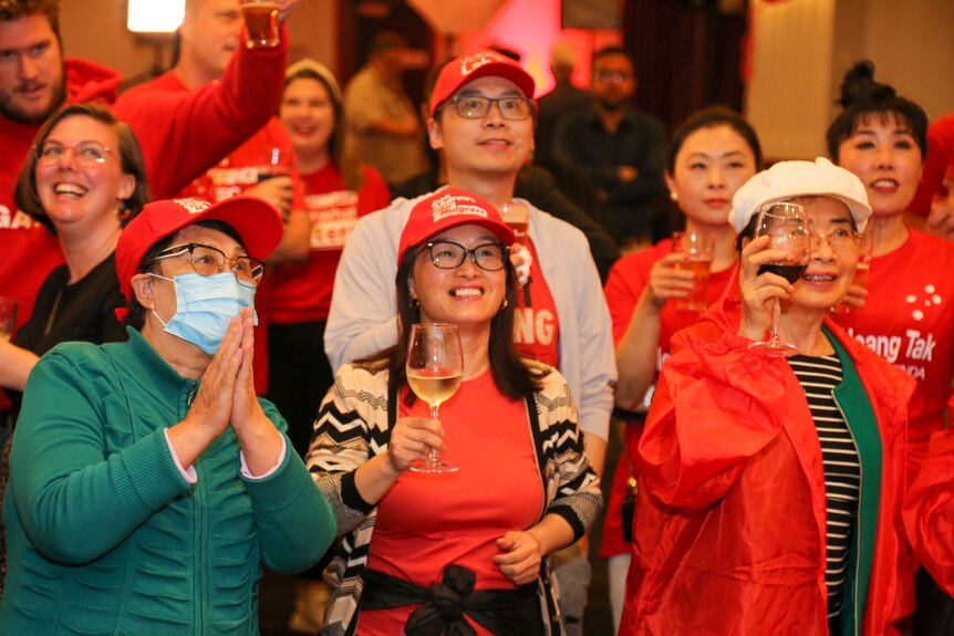 A group of people in Labor red smile and hold their drinks as they celebrate on election night
