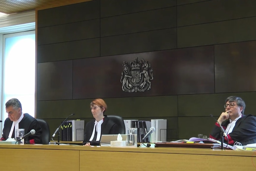 A screenshot of a web stream shows a man, a woman and another man sitting on judges benches.