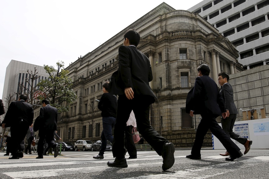 Men in black suits walk along a pedestrian crossing in front of an old building,