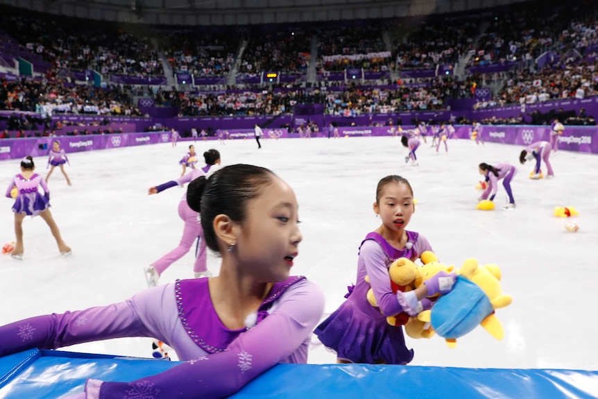 Skating girls collect Winnie the Pooh toys thrown on the ice during men's figure skating.