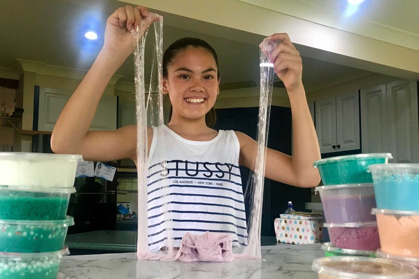 A young girl stretches slime from the table top to above her head