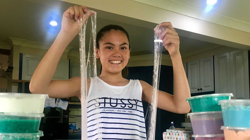 A young girl stretches slime from the table top to above her head