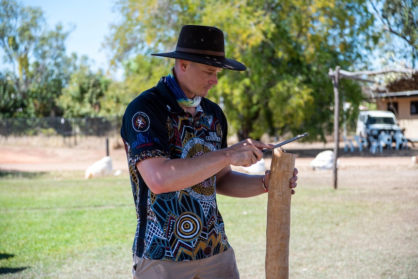 A man in a hat files a Didgeridoo at Barunga.