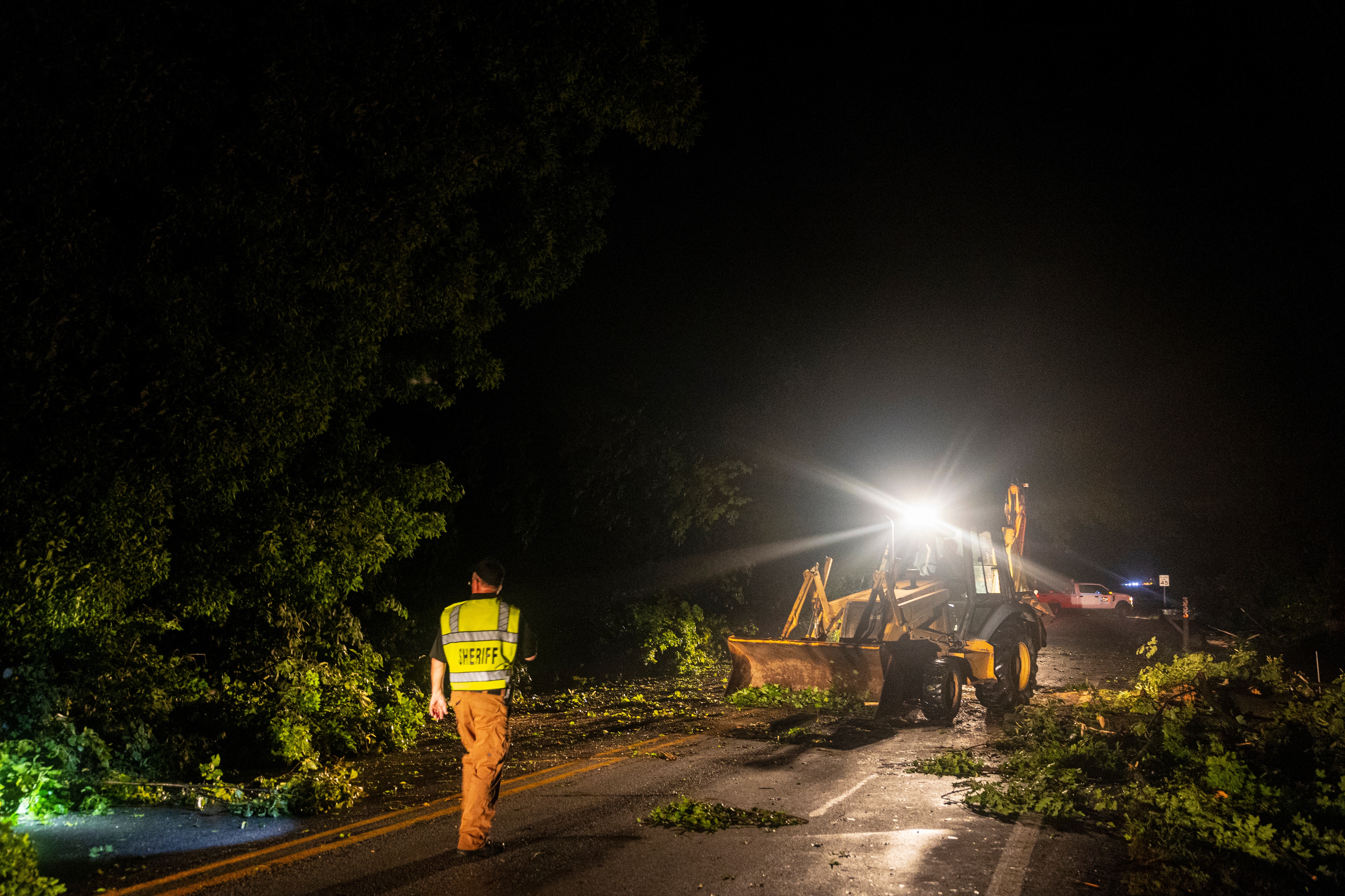 Emergency worker in high-vis clothing on a road with fallen trees and a truck clearing it