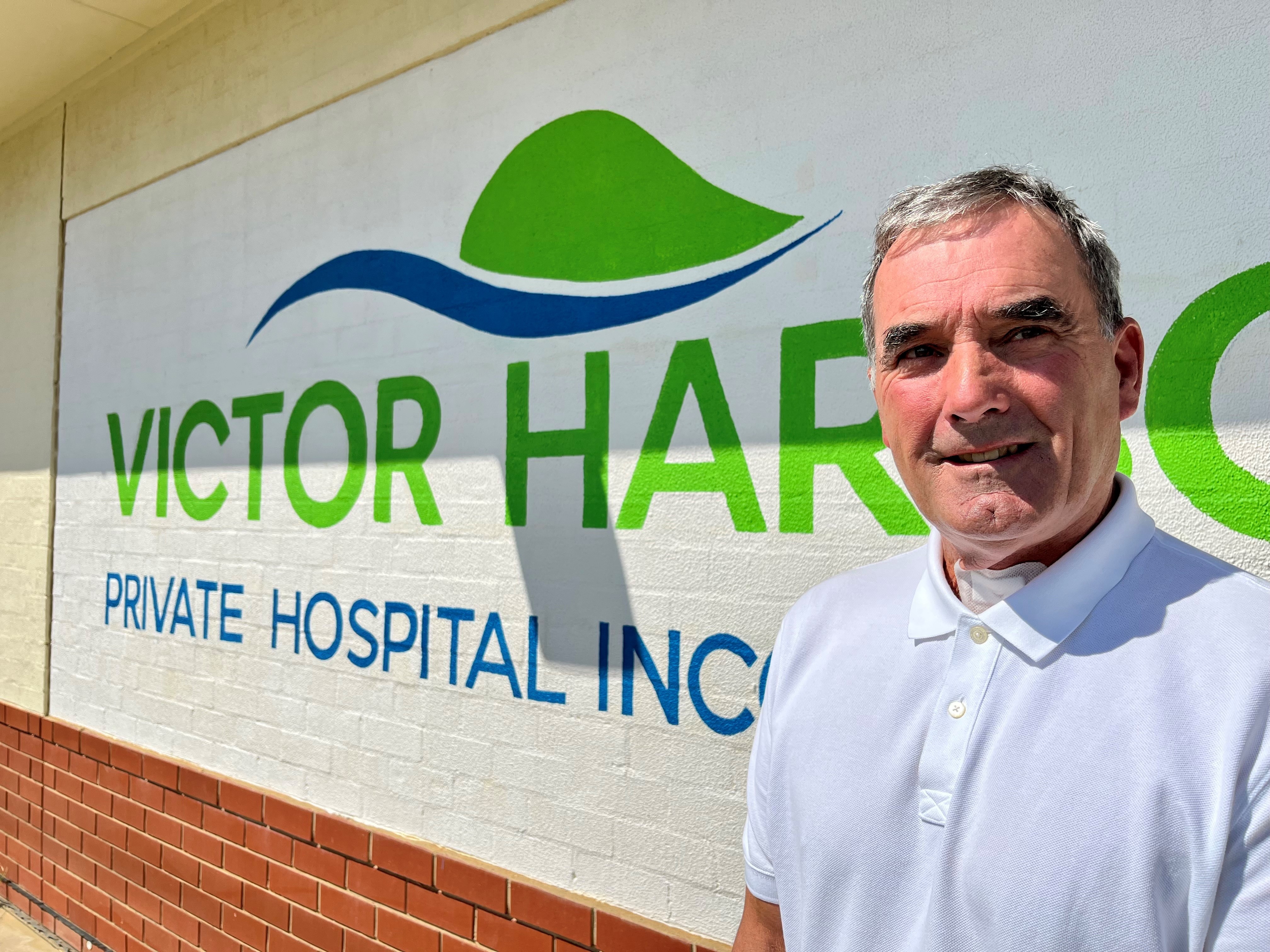 A man stands in front of a sign that reads Victor Harbor Private Hospital