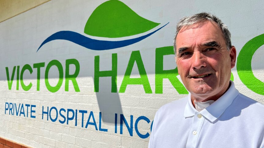 A man stands in front of a sign that reads Victor Harbor Private Hospital