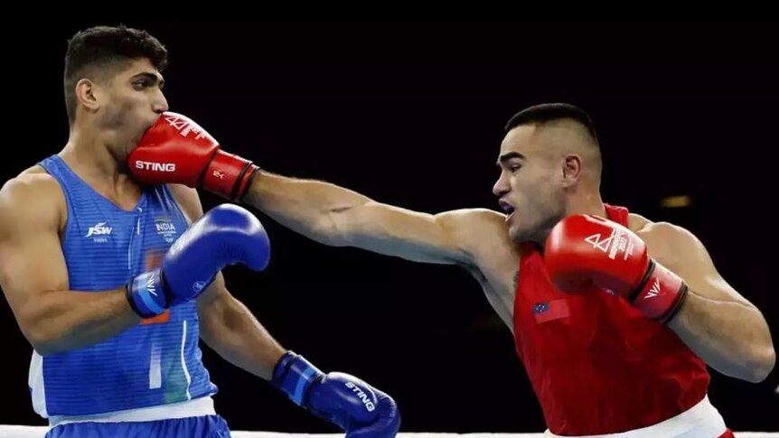Boxer wearing red extends right gloved arm knocking opponent in blue in mouth. Both boxers are in the ring. 