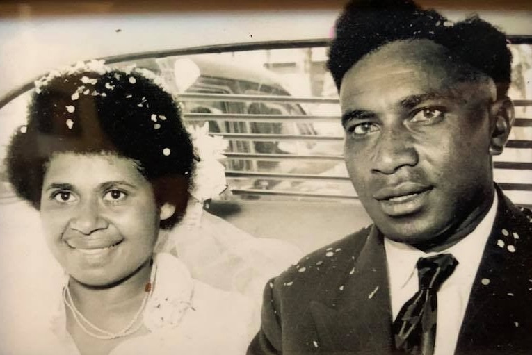 Black and white photo of a young Australian South Sea Islander couple in the back of a car on their wedding day.