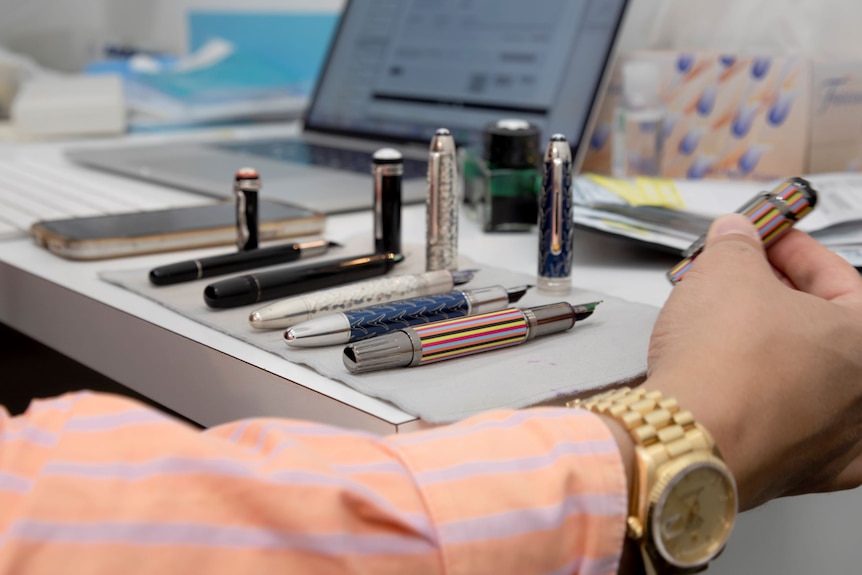 A row of fountain pens in various styles and colours sits on a desk.