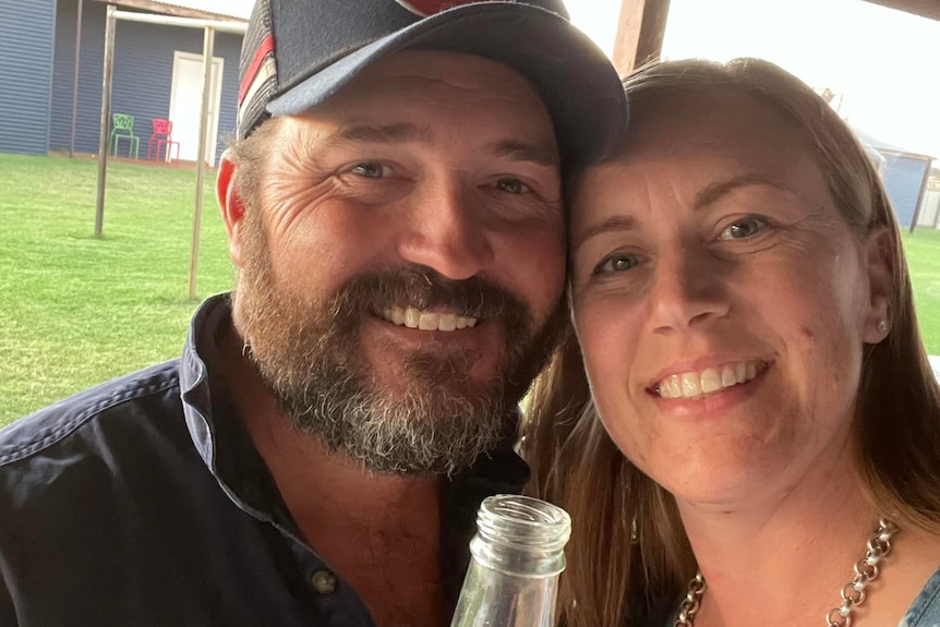 A white man with a beard and a white woman smile and take a selfie holding a drink. 