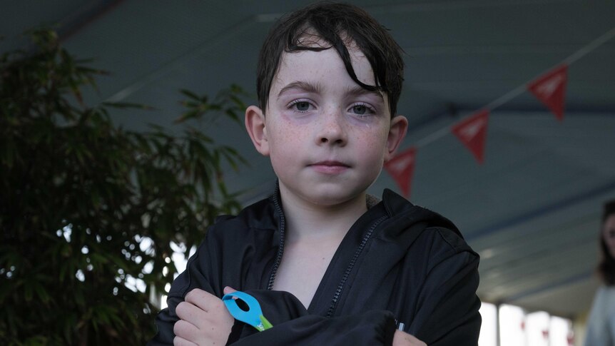 Parker stands in the doorway of an indoor pool with wet hair and a towel wrapped around him. 