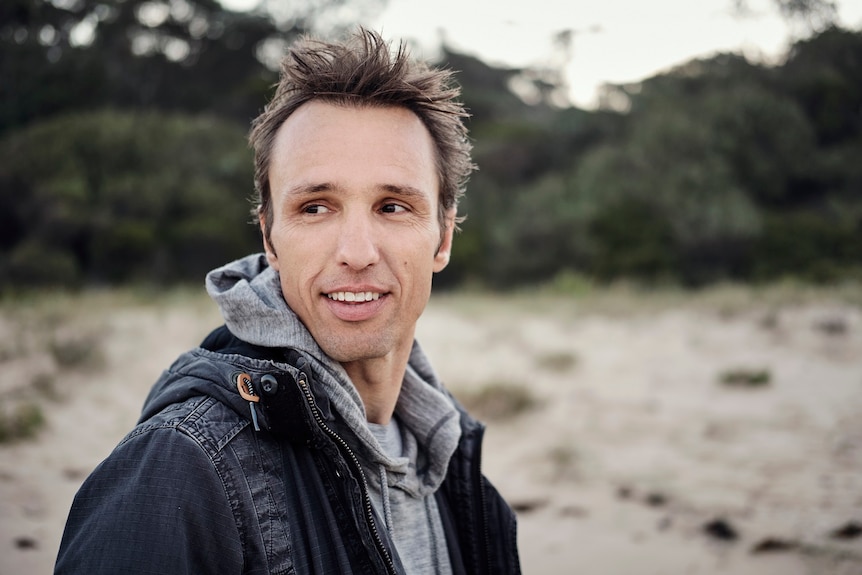 A smiling man stands on a beach