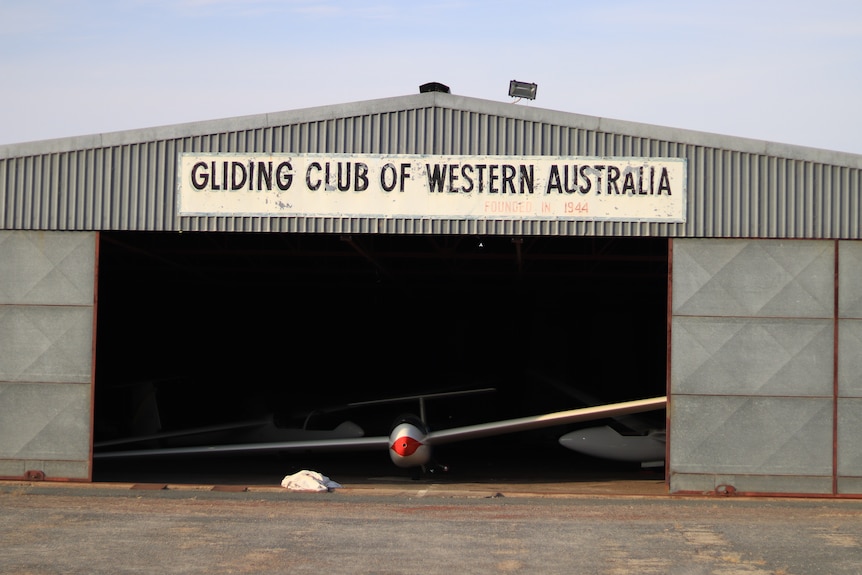 An old rusty hanger with a glider plane poking its nose out.