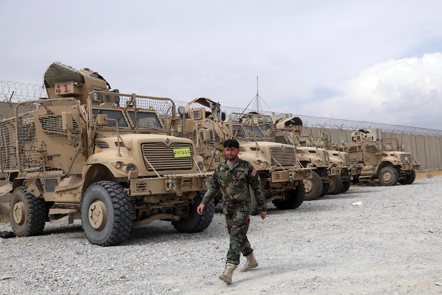 A soldier walks past five army vehicles. 
