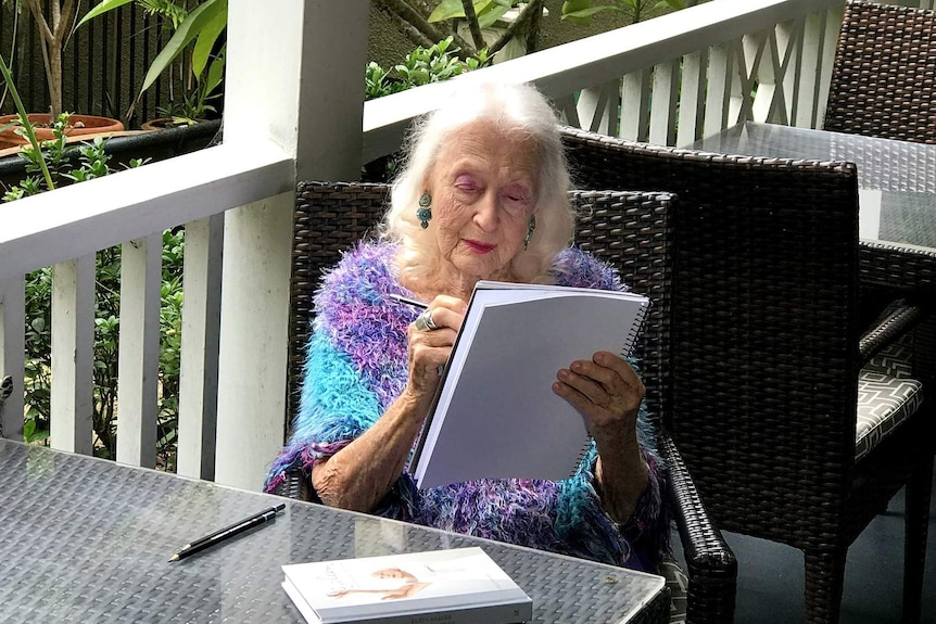 A woman sitting at a table draws on a sketch pad.