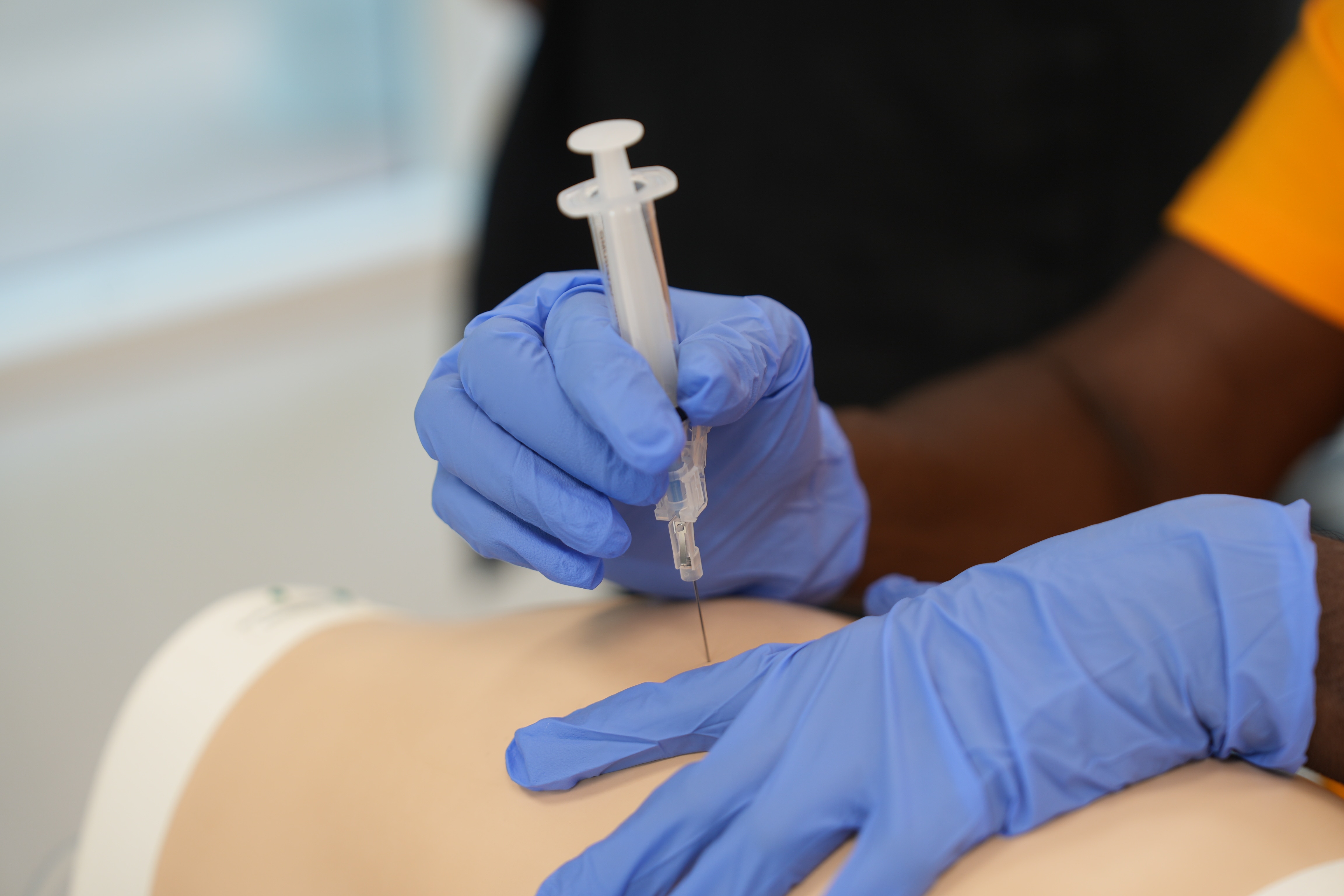 A close-up of gloved hands administering a needle into a test dummy.
