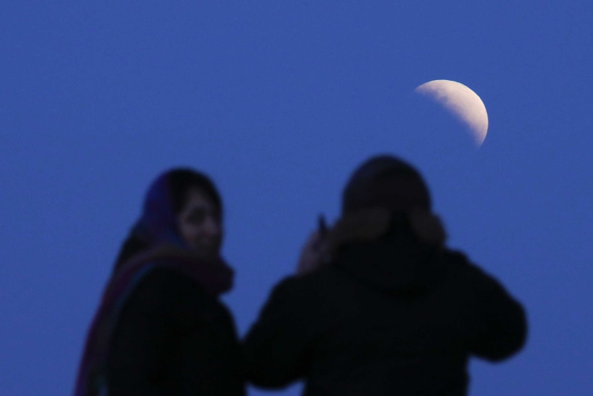 A couple is silhouetted while watching a lunar eclipse