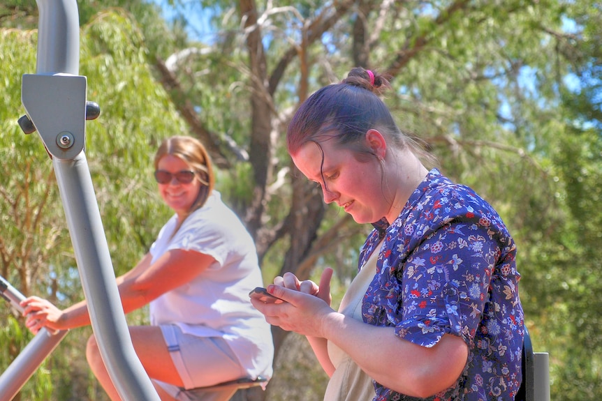 Kylie looking over at Siahn smiling as she looks at her phone