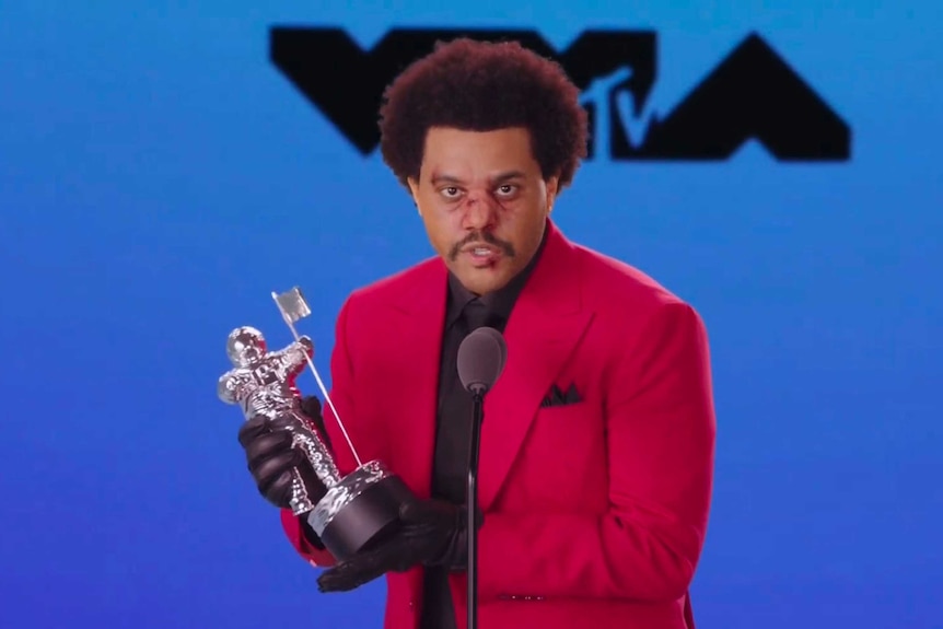 Singer The Weeknd accepts the video of the year award he is wearing a red suit jacket