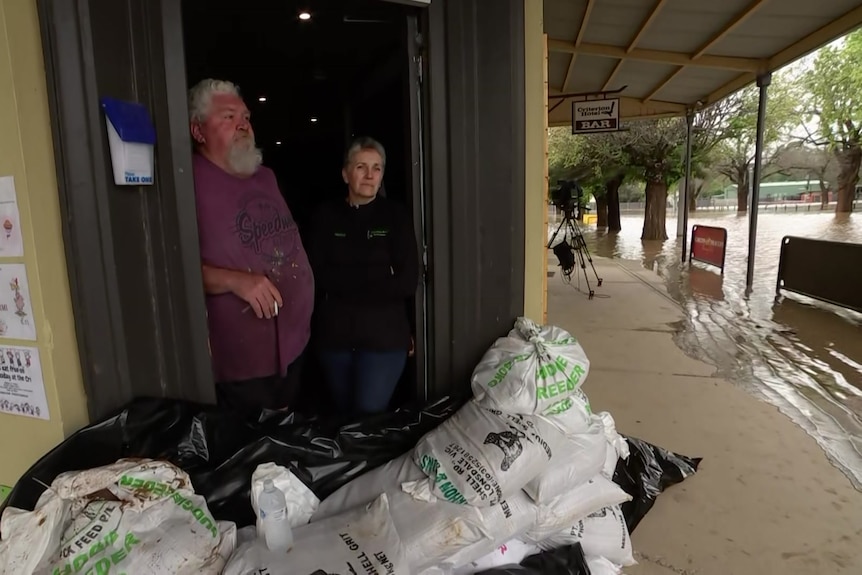 Craig and Teresa lean against the doorframe of their pub which is sandbagged as floodwater covers the footpath